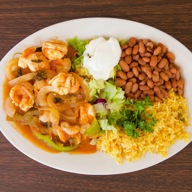 Shrimp fajitas with onions and peppers, served with rice, beans, lettuce, and sour cream.