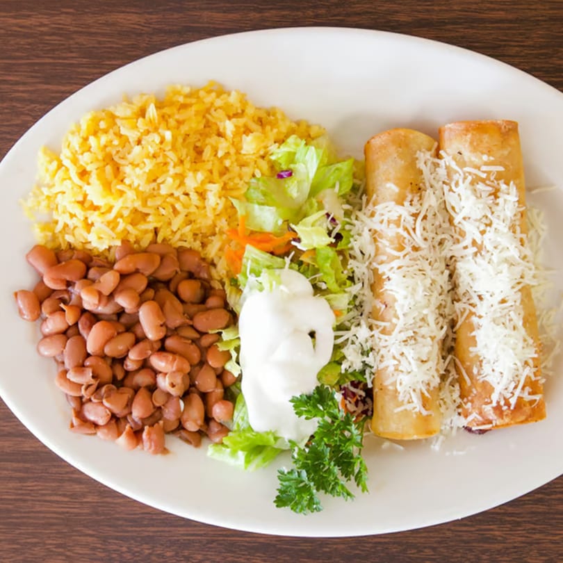 Taqueria Morena's Mexican dish with two flautas, rice, pinto beans, salad, sour cream, and parsley.