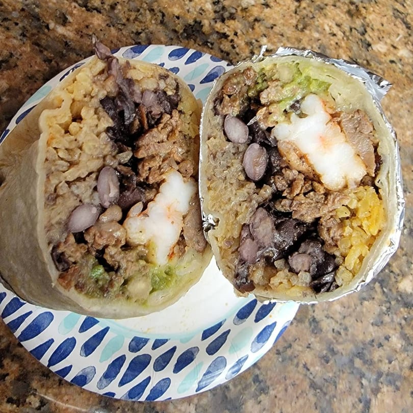 A large Taqueria Morena burrito, cut in half, revealing shrimp, rice, beans, and meat.